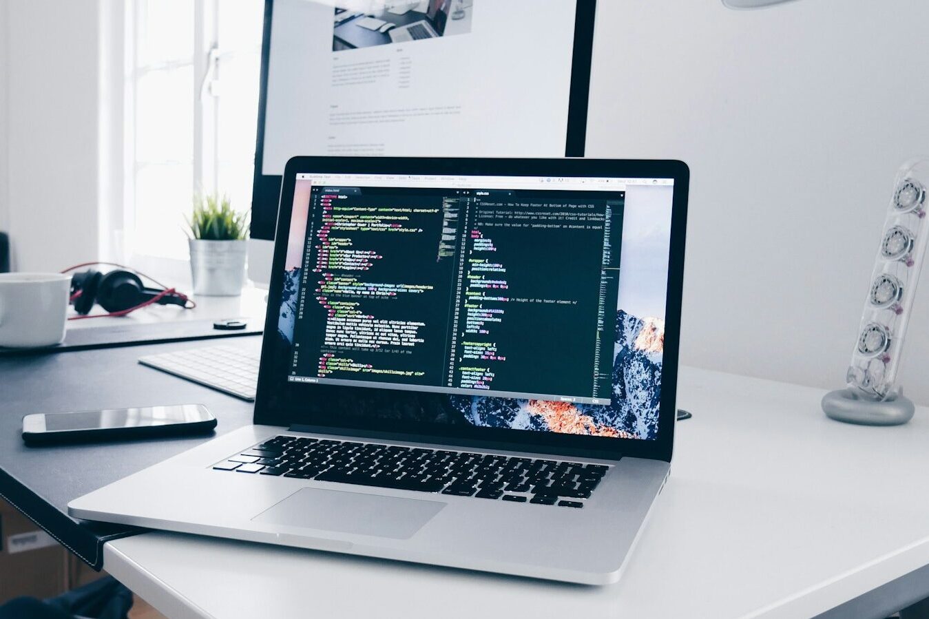 A MacBook with lines of code on its screen on a busy desk